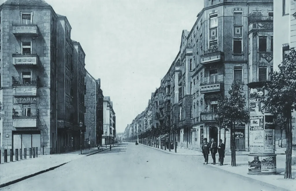 1918. Blick in die 1906 benannte und um 1910 bebaute Simplonstraße von der Ecke Lenbachstraße aus. Rechts Nr. 1 die Eckkneipe „Zum weissen Hirsch“ von Gastwirt Carl Seggedi, der in der Nr. 5 noch einen Zigarrenladen besaß. Links hinter dem Eckhaus der Kohlenplatz (Nr. 44) von August Miehl. Er wohnte gegenüber in der Nr. 3.